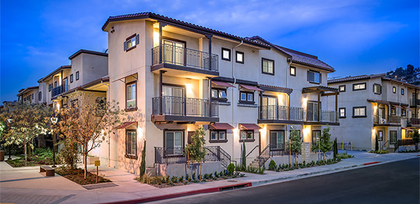 Evening view of three-story stucco apartment buildings with tile roofs, balconies, and landscaping.